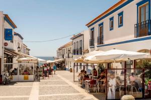 a street with people sitting at tables and umbrellas at Casa da Praia em Porto Côvo in Porto Covo
