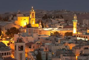 un perfil urbano por la noche con una torre de reloj en Holy Land Hotel, en Bethlehem