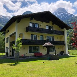 a large yellow house with mountains in the background at Landhaus Lilly in Obertraun