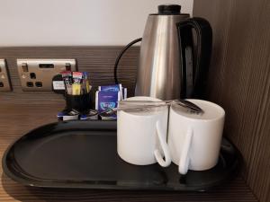 ロンドンにあるザ ビバリー ホテル ロンドン ヴィクトリアのカウンターの上に置かれた2つの白いカップとコーヒーポット