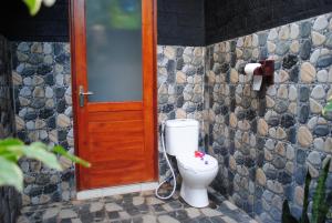 a bathroom with a toilet and a wooden door at Tiara Homestay Pemuteran Bali in Pemuteran