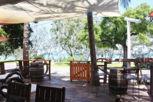 eine Terrasse mit Tischen, Stühlen und einem Sonnenschirm in der Unterkunft Arcadia Beach Guest House and Car Hire in Nelly Bay