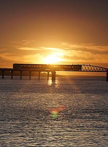 a train crossing a bridge over the water at sunset at Awel Y Mor in Barmouth