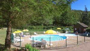 una valla alrededor de una piscina con sombrillas y sillas en VVF Cantal Champs-sur-Tarentaine, en Champs Sur Tarentaine