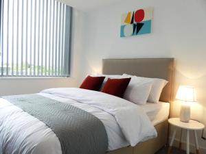 a bedroom with a bed with white sheets and red pillows at Basingstoke Apartments - Downtown Luxury Apartments in Basingstoke