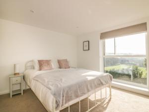 a white bedroom with a bed and a window at The Beach Halt in Perranporth