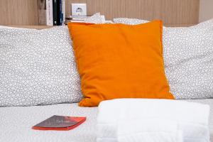 uma almofada laranja e um livro numa cama em Heart of Aveiro Apartment em Aveiro