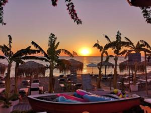 a beach with a boat with palm trees and the sunset at Tsambikos Apts in Faliraki