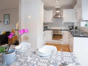 a kitchen with white cabinets and a table with pink flowers at Coed y Felin in Conwy