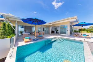 a house with a swimming pool and two umbrellas at Single Level BEACHSIDE VILLA - BB2 - at BAYSIDE LUXURY VILLAS Samrong Bay Beach, 3 BED 4 BATH, SEA and SUNSET VIEWS, only 200m walk to the Beach in Bang Rak Beach