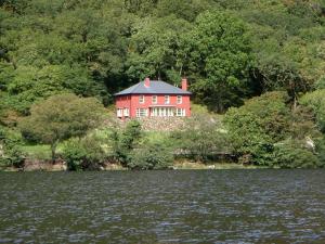 a red house on the shore of a body of water at Dinas Noddfa in Beddgelert