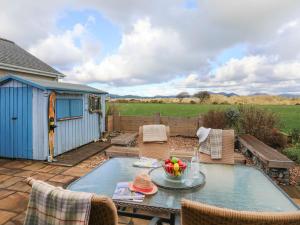 un patio con mesa y sillas y un cobertizo azul en Dwyros, en Pwllheli