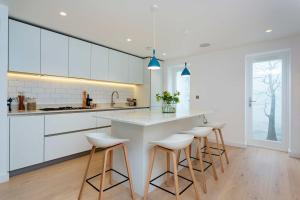a kitchen with white cabinets and a counter with stools at Veeve - Princedale Road Minimalism in London