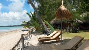 a beach with chairs and a hammock and the ocean at Pousada Doze Cabanas in Japaratinga