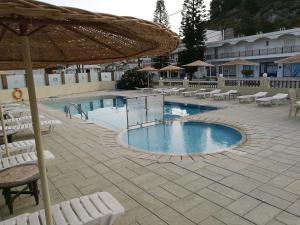 a swimming pool with white chairs and an umbrella at Golden days in Afantou