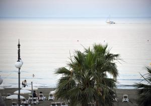 a beach with a palm tree and chairs and a boat in the water at Hai Hotel in Larnaca