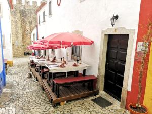 a row of tables with red umbrellas on a street at Foral Guest House - Óbidos in Óbidos