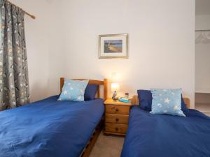 two beds in a bedroom with blue sheets and a night stand at Mwythus in Rhoscolyn