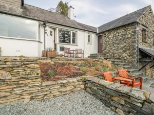 a stone house with a stone wall and two chairs at Kirkstone Cottage in Ambleside