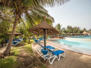 eine Gruppe von Stühlen und Sonnenschirmen neben einem Pool in der Unterkunft Senegambia Beach Hotel in Sere Kunda NDing