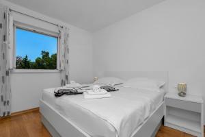 a white bedroom with a bed and a window at Apartman Jug in Makarska
