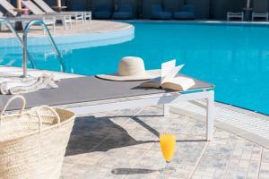 a table with a hat and a book next to a pool at Princess Golden Beach Hotel in Chrysi Ammoudia