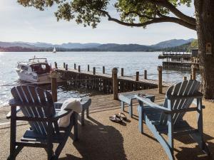 two chairs and a table next to a dock with a boat at Waterhead Cottage in Windermere