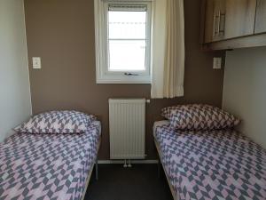 two beds in a room with a window and a radiator at Chalet 15 (Resort Venetië) in Giethoorn
