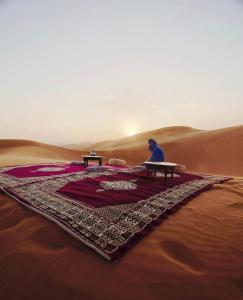 a man sitting on a table in the desert at Sahara Tours luxury camp in Merzouga