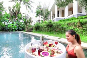 una mujer sentada en una mesa con una bandeja de comida junto a una piscina en Villa Cinta Ubud, en Ubud