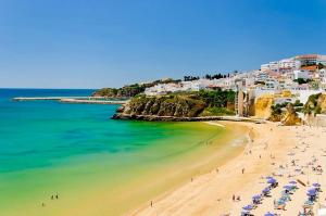 a beach with people and umbrellas and the ocean at Quinta Barracuda Albufeira in Albufeira