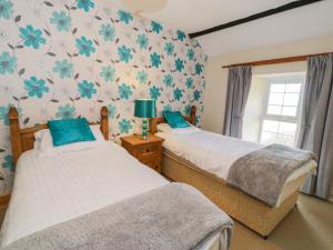 2 Betten in einem Schlafzimmer mit blauen Blumen an der Wand in der Unterkunft The Stable Cottage in Llanbedr