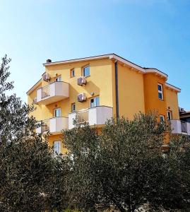 ein gelbes Gebäude mit Balkonen und Bäumen davor in der Unterkunft Apartmani Lili in Sukošan