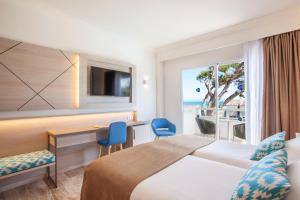 a hotel room with a bed and a desk and a window at Grupotel Los Príncipes & Spa in Playa de Muro