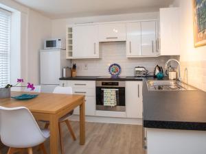 a kitchen with white cabinets and a wooden table at Bryn Teg Cottage in Menai Bridge