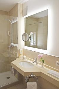 ein Bad mit einem Waschbecken, einer Dusche und einem Spiegel in der Unterkunft Hotel Fischerhaus in Starnberg