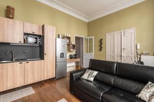 a living room with a black leather couch and a kitchen at Le cœur de Reims, la mairie et le Boulingrin in Reims