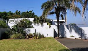 a white fence with palm trees in front of a house at African Sands B&B in Amanzimtoti