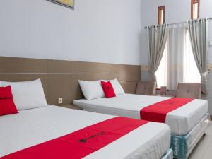 two beds in a hotel room with red and white sheets at RedDoorz near Goa Panggung in Pangandaran