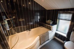 a bath tub in a bathroom with black tiled walls at Madoc Brook Cottage in Conwy