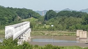 a bridge over a river with a lighthouse in the distance at The Guesthouse DMZ Stay in Paju