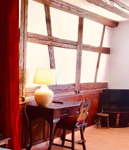 einem Tisch mit einer Lampe und einem Stuhl vor einem Fenster in der Unterkunft AUX DEUX CIGOGNES AMMERSCHWIHR in Ammerschwihr