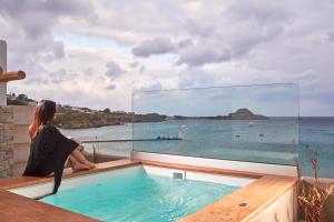 a woman sitting in a hot tub looking out at the ocean at Kosmoplaz Beach Hotel in Platis Yialos Mykonos