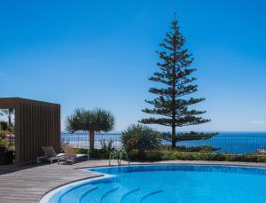 a swimming pool with a pine tree next to the ocean at Hotel Do Campo in Ribeira Brava