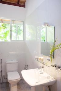 a white bathroom with a sink and a toilet at Alvas house in Hikkaduwa