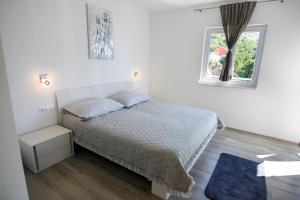a white bedroom with a bed and a window at Apartmani Ticinovic in Omiš