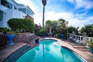 a swimming pool in a yard with chairs and a palm tree at A Heavenly View in Muizenberg