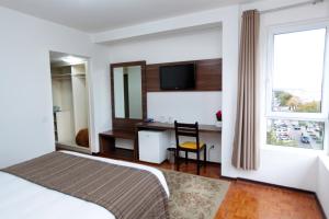 a bedroom with a bed and a desk and a window at Hotel Obino Bagé in Bagé