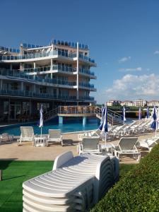 a pool with lounge chairs and a large building at DEA Pasavan Apartments in Ravda