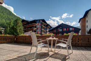 2 chaises et une table sur une terrasse avec un bâtiment dans l'établissement Hotel Astoria, à Zermatt